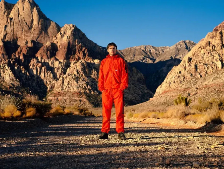 Man in an orange Pro Club tracksuit on a desert trail below red rock cliffs