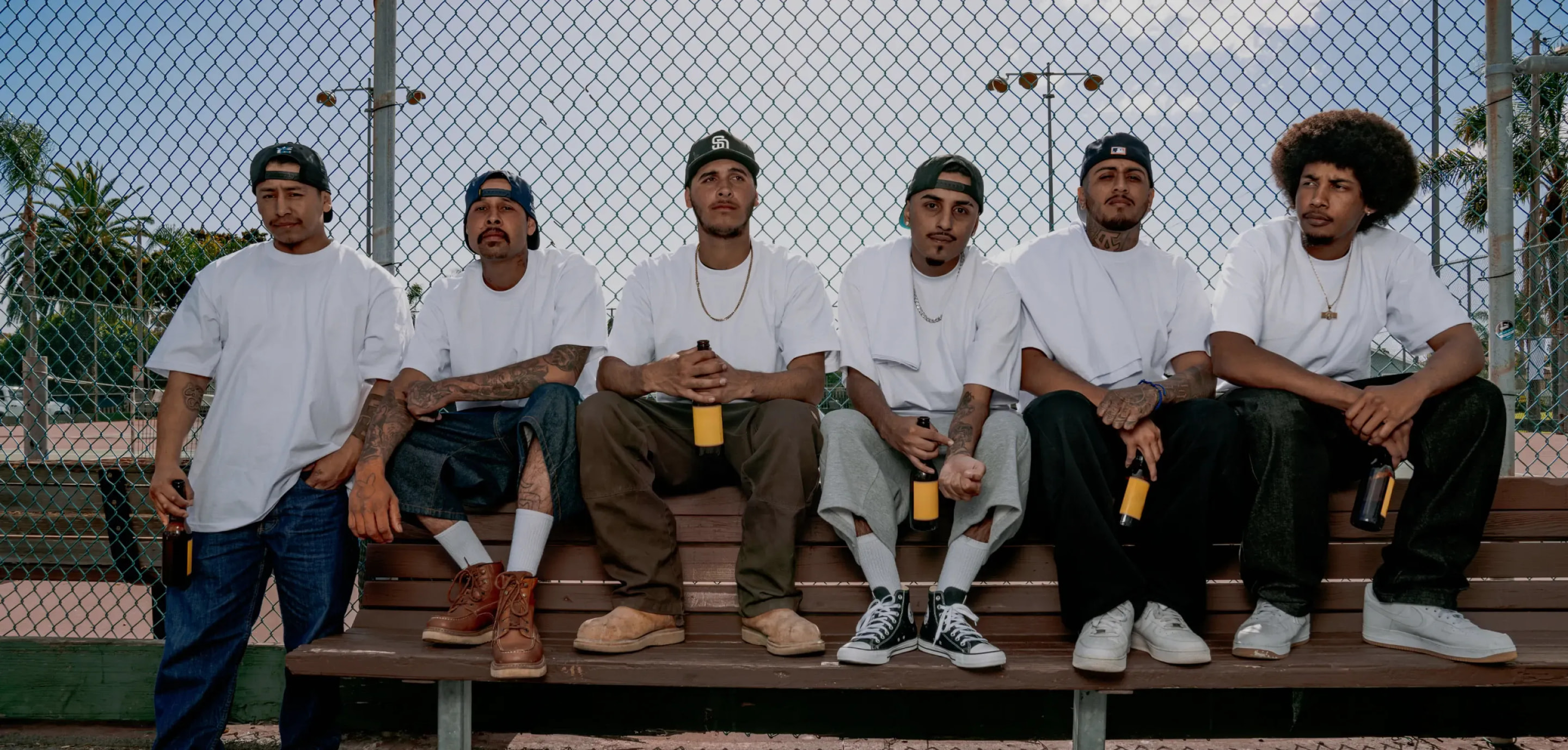 Group of men seated on a bench by a chain-link fence — Pro Club community