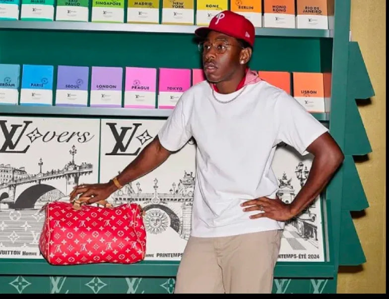 Tyler, The Creator in a white t-shirt and red cap holding a red bag