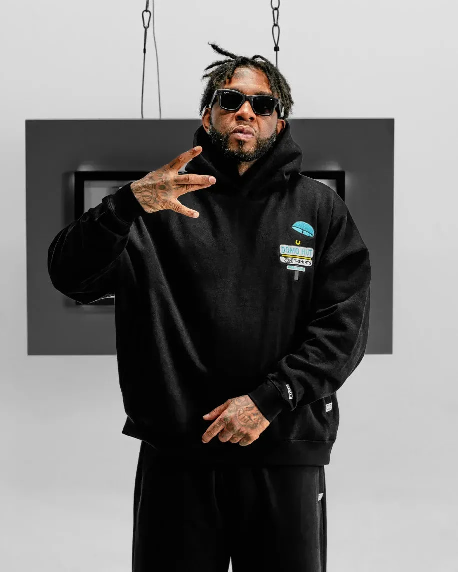 Man in a black Pro Club hoodie throwing a hand sign