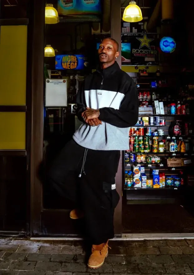 Man in a grey-and-black Pro Club quarter-zip outside a corner store at night